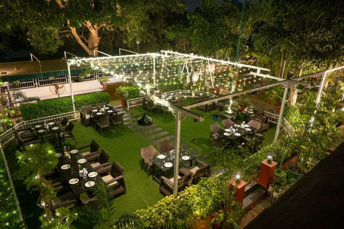 The garden at night from above, tables on the lawn beneath a canopy of string lights
